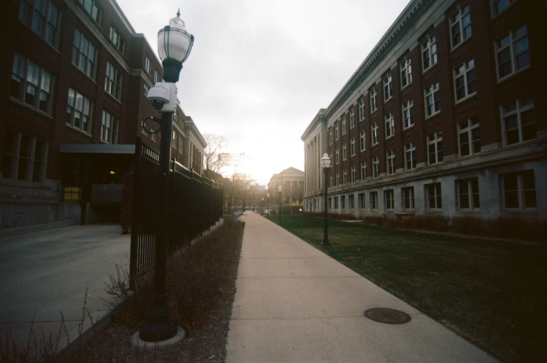 A path cutting down a courtyard with a building on the left and right and a streetlamp in the foreground.